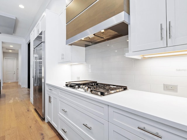 kitchen with decorative backsplash, appliances with stainless steel finishes, custom exhaust hood, white cabinets, and light hardwood / wood-style floors