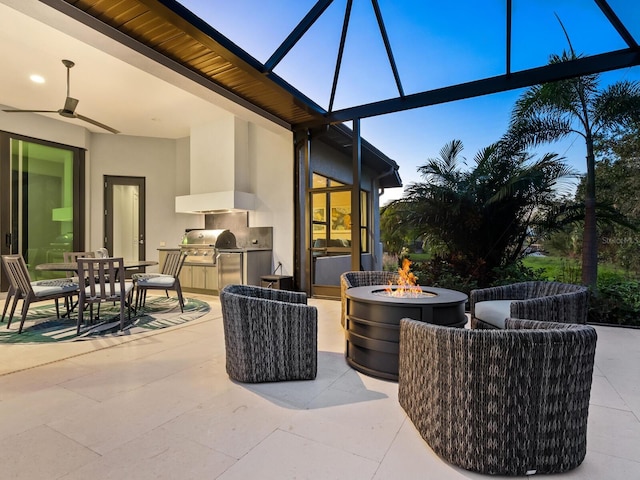 patio terrace at dusk with a fire pit, an outdoor kitchen, area for grilling, and a lanai