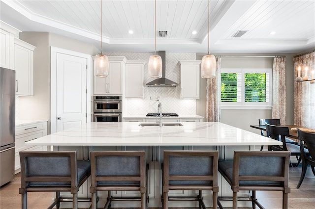 kitchen featuring pendant lighting, a raised ceiling, a spacious island, wall chimney range hood, and a breakfast bar area