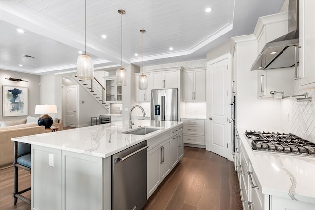 kitchen with sink, stainless steel appliances, wall chimney range hood, a spacious island, and decorative light fixtures