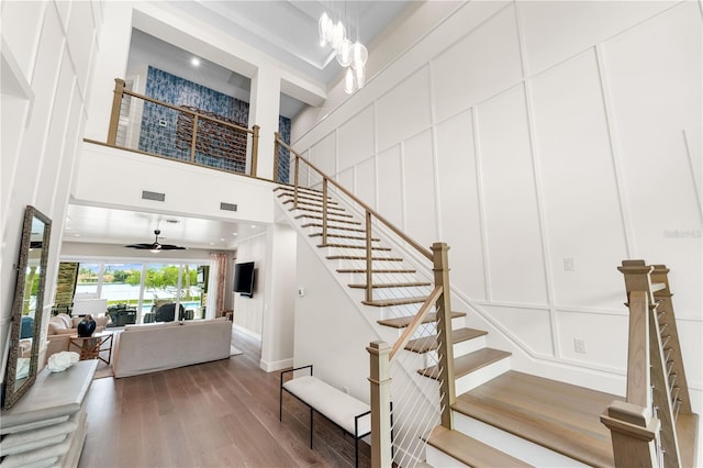 staircase with ceiling fan with notable chandelier, hardwood / wood-style floors, and a towering ceiling