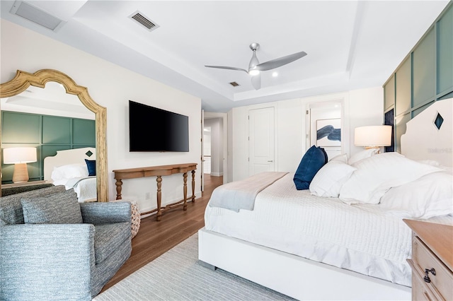 bedroom with hardwood / wood-style floors, a raised ceiling, and ceiling fan