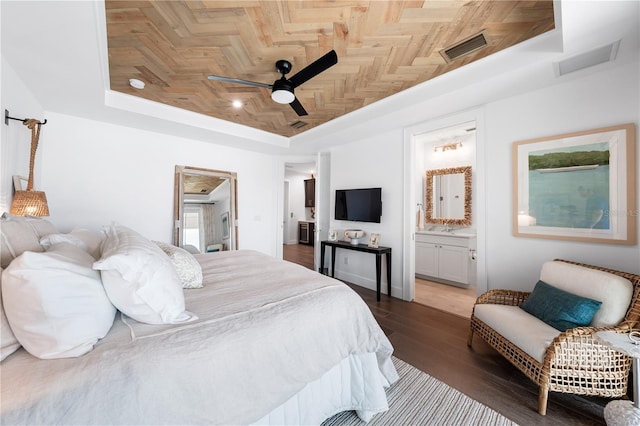 bedroom with a raised ceiling, ceiling fan, dark hardwood / wood-style flooring, and ensuite bath