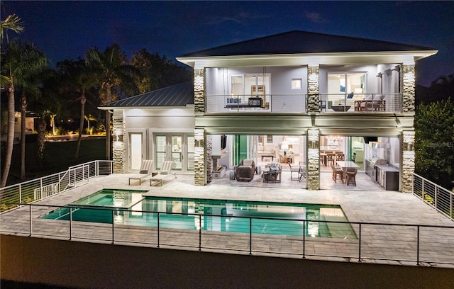 back house at twilight featuring a balcony, a patio area, and a pool with hot tub