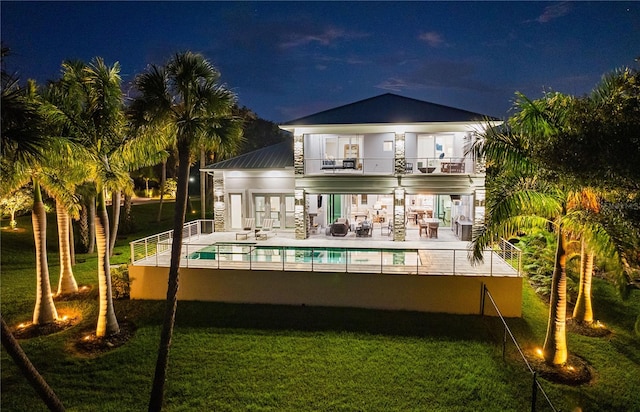 back house at night with french doors, a patio, a balcony, and a lawn