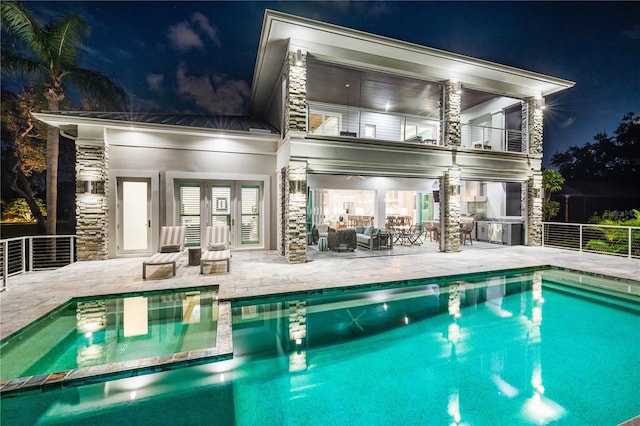 back house at night featuring a patio area, an outdoor living space, a balcony, and french doors