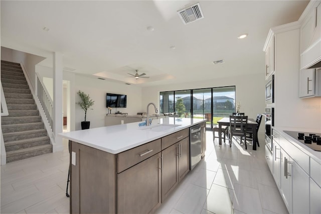 kitchen with stainless steel appliances, ceiling fan, sink, white cabinets, and an island with sink