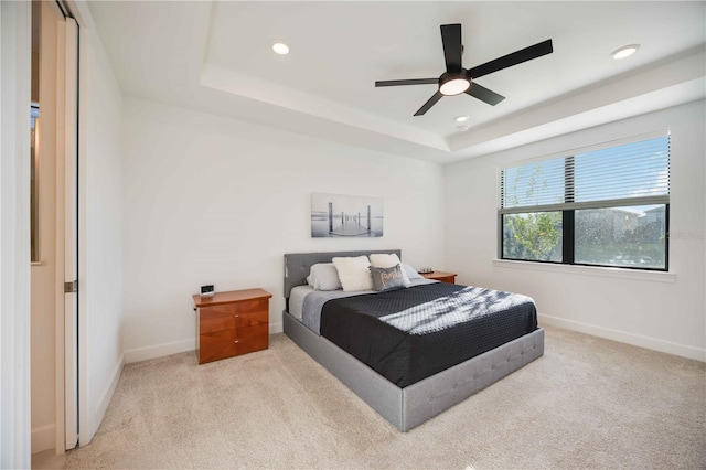 bedroom featuring ceiling fan, light colored carpet, and a tray ceiling