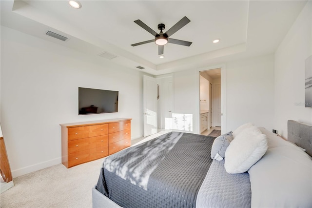 carpeted bedroom with a tray ceiling, connected bathroom, and ceiling fan