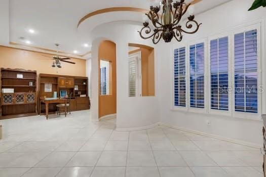 tiled empty room with ceiling fan with notable chandelier