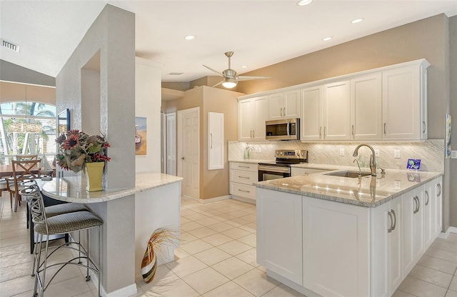 kitchen with kitchen peninsula, light stone countertops, stainless steel appliances, sink, and white cabinets