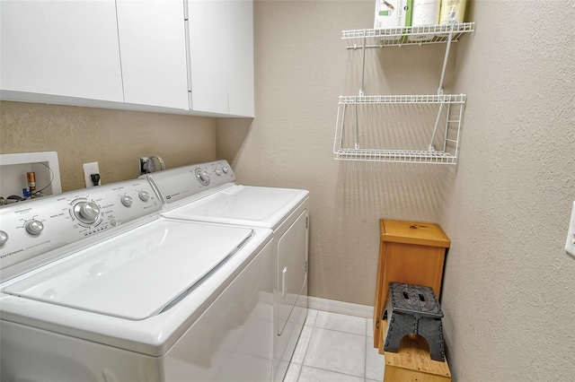 clothes washing area featuring cabinets, light tile patterned floors, and washing machine and dryer