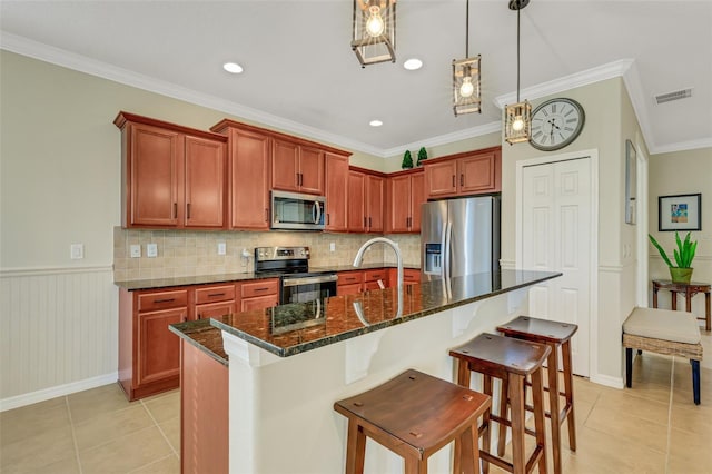 kitchen featuring ornamental molding, an island with sink, appliances with stainless steel finishes, and dark stone counters