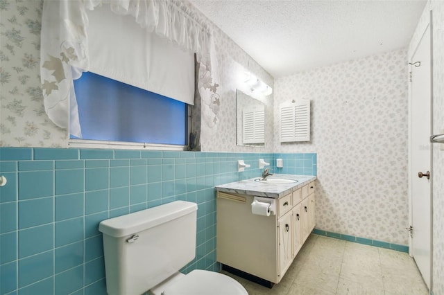 bathroom with vanity, toilet, a textured ceiling, and tile walls