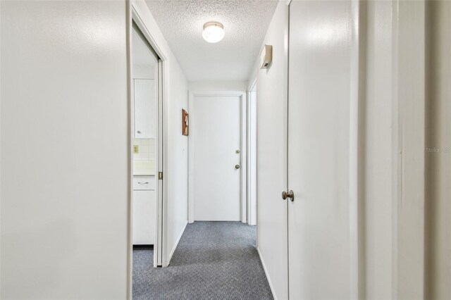 hallway with dark carpet and a textured ceiling