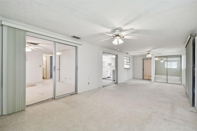 spare room with a textured ceiling, light colored carpet, and ceiling fan