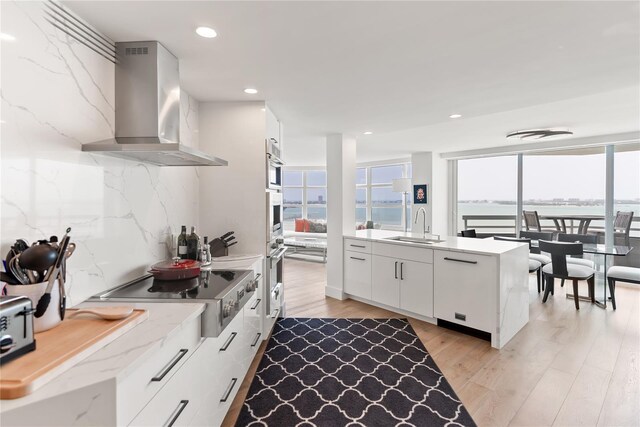 kitchen featuring backsplash, white cabinets, wall chimney exhaust hood, and a healthy amount of sunlight