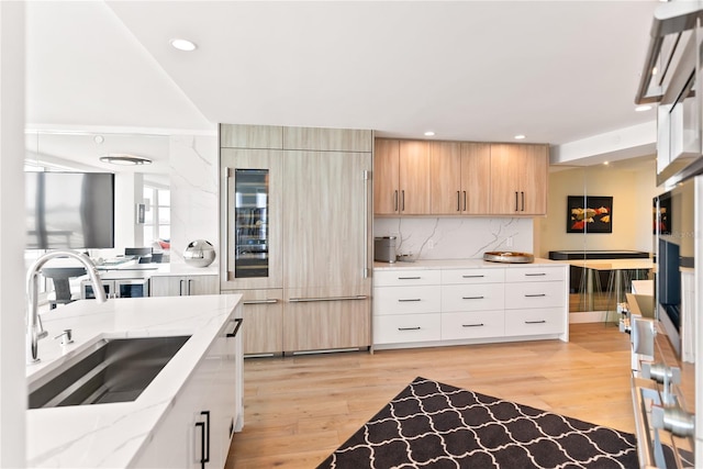 kitchen with light stone countertops, light brown cabinetry, sink, light hardwood / wood-style flooring, and built in fridge