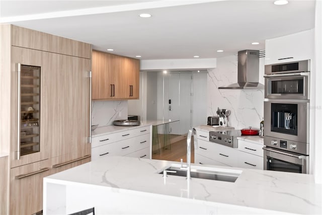 kitchen featuring white cabinets, sink, tasteful backsplash, and wall chimney range hood