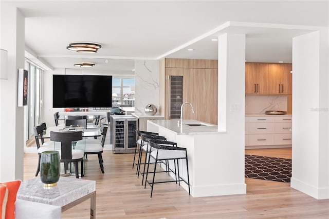 kitchen featuring decorative backsplash, a kitchen breakfast bar, sink, light hardwood / wood-style flooring, and wine cooler