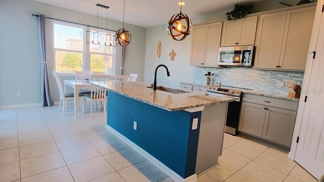 kitchen featuring an island with sink, light stone counters, a sink, stainless steel appliances, and backsplash