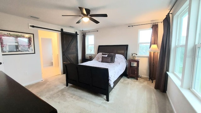 bedroom featuring a barn door, light carpet, visible vents, baseboards, and ensuite bath