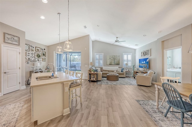 kitchen featuring sink, vaulted ceiling, light wood-type flooring, an island with sink, and a breakfast bar area