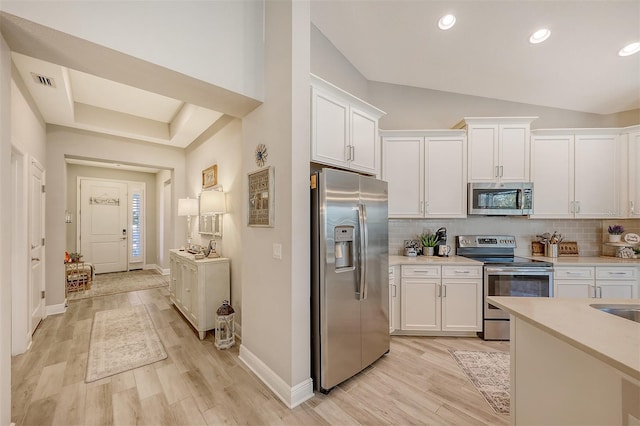 kitchen featuring vaulted ceiling, stainless steel appliances, white cabinetry, and light hardwood / wood-style floors