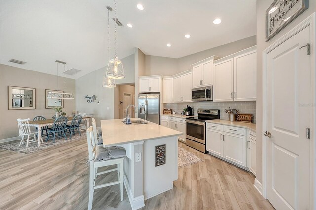 kitchen featuring white cabinets, a center island with sink, sink, appliances with stainless steel finishes, and decorative light fixtures