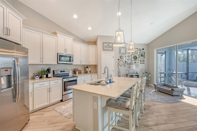 kitchen with white cabinets, stainless steel appliances, a kitchen island with sink, and lofted ceiling