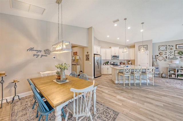 dining room with high vaulted ceiling and light hardwood / wood-style flooring