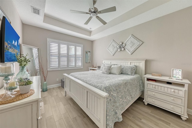 bedroom featuring a tray ceiling, ceiling fan, and light hardwood / wood-style flooring