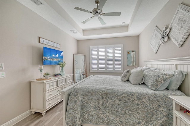 bedroom with light hardwood / wood-style floors, ceiling fan, and a tray ceiling