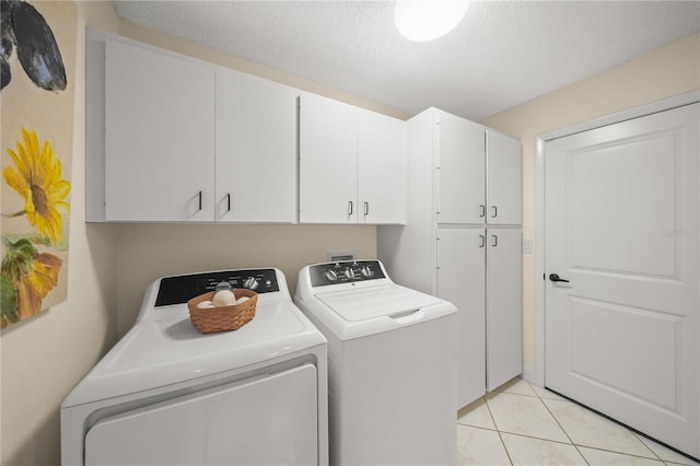 laundry room featuring cabinets, light tile patterned floors, a textured ceiling, and washer and clothes dryer