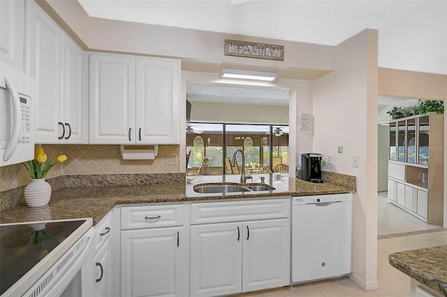 kitchen featuring white appliances, a sink, white cabinetry, decorative backsplash, and dark stone counters