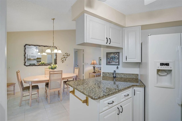 kitchen with light tile patterned floors, white appliances, white cabinetry, hanging light fixtures, and dark stone countertops