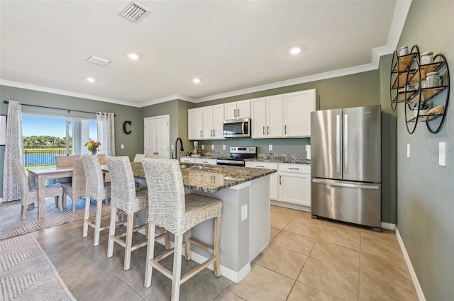 kitchen featuring appliances with stainless steel finishes, a kitchen island with sink, dark stone countertops, white cabinetry, and a breakfast bar area