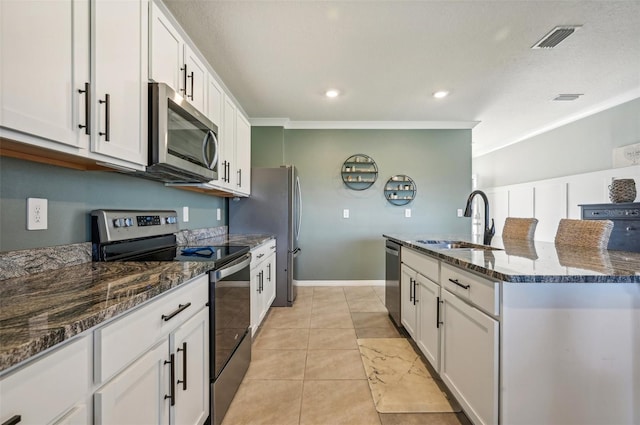 kitchen with appliances with stainless steel finishes, dark stone counters, sink, light tile patterned floors, and white cabinetry