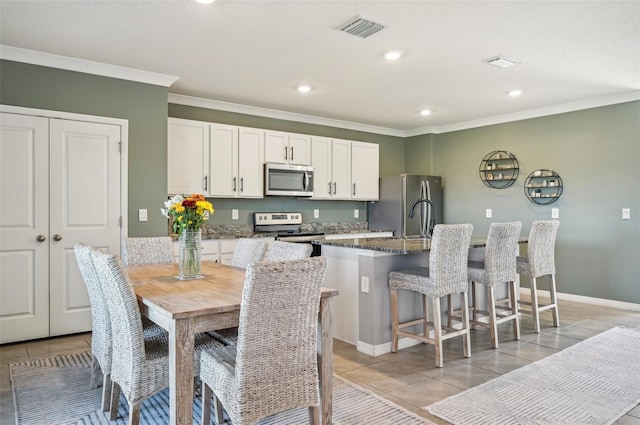 kitchen featuring light tile patterned floors, dark stone counters, a kitchen island with sink, white cabinets, and appliances with stainless steel finishes