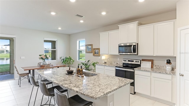 kitchen with white cabinets, plenty of natural light, stainless steel appliances, and an island with sink