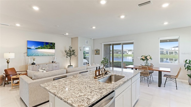 kitchen with light stone countertops, sink, white cabinetry, and an island with sink