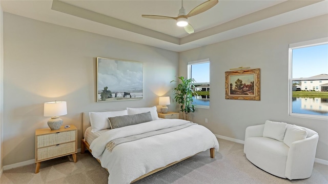 carpeted bedroom with a raised ceiling, multiple windows, ceiling fan, and a water view