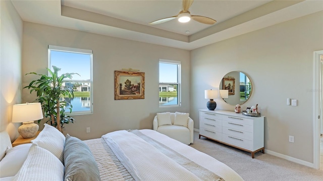 bedroom featuring a tray ceiling, ceiling fan, a water view, and light carpet