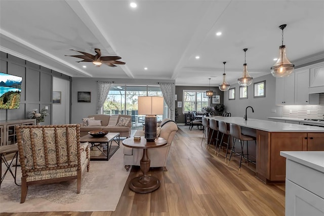 living room featuring light hardwood / wood-style floors, sink, ornamental molding, ceiling fan, and beam ceiling