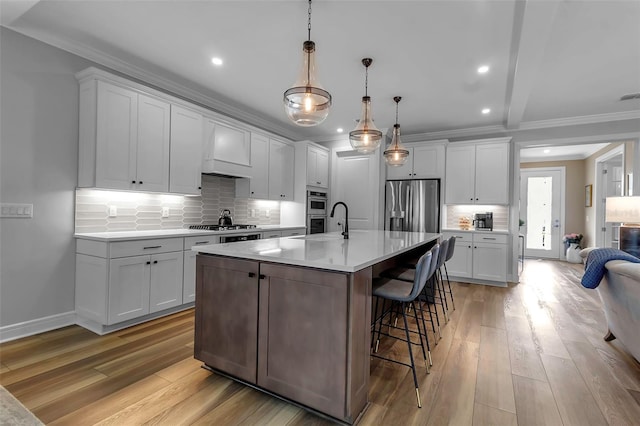 kitchen with appliances with stainless steel finishes, a kitchen island with sink, white cabinets, light hardwood / wood-style flooring, and pendant lighting