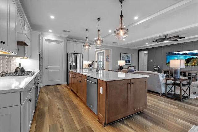 kitchen featuring a kitchen island with sink, white cabinets, sink, pendant lighting, and stainless steel appliances