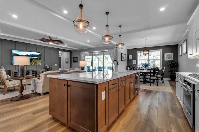 kitchen featuring oven, light hardwood / wood-style floors, a kitchen island with sink, sink, and decorative light fixtures