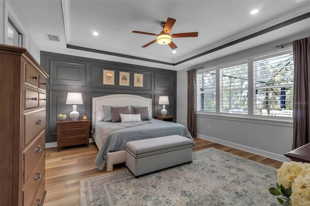 bedroom with crown molding, hardwood / wood-style flooring, a tray ceiling, and ceiling fan