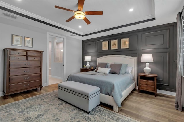 bedroom featuring wood-type flooring, ceiling fan, ensuite bathroom, a tray ceiling, and ornamental molding