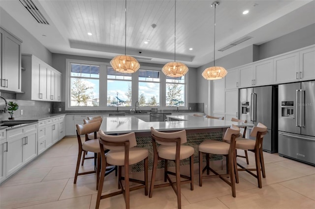 kitchen with a spacious island, backsplash, a breakfast bar, a tray ceiling, and high end fridge